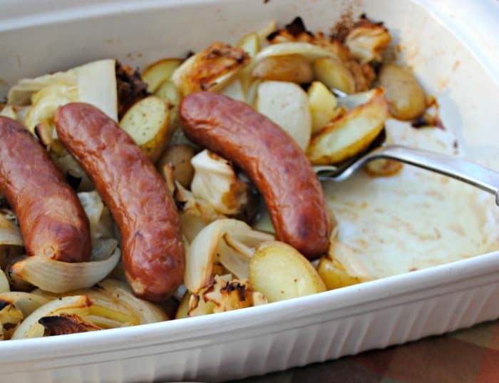 sausage links, onions, potatoes, and cabbage in a white casserole dish