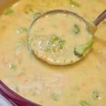 ladle scooping broccoli cheddar soup from a red pot