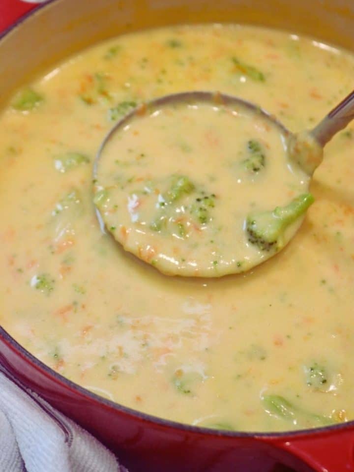 ladle scooping broccoli cheddar soup from a red pot