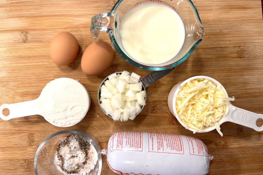 eggs, milk, flour, onion, cheddar cheese, spices, and ground beef on a wooden cutting board