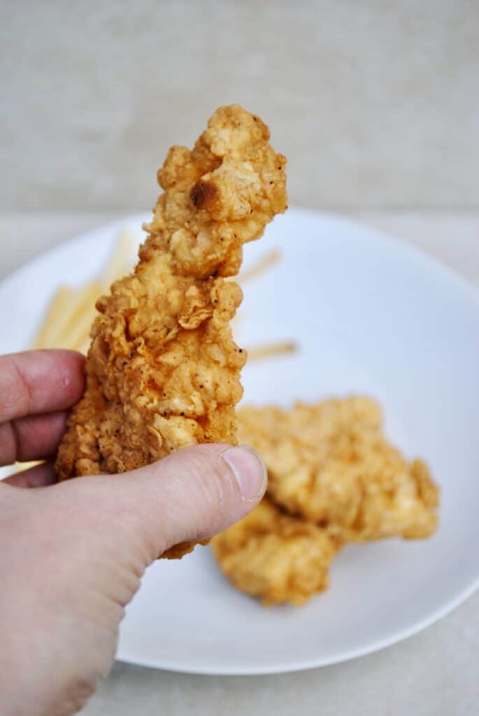 Hand holding a crispy chicken strip