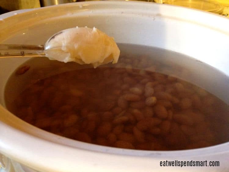 tablespoon of fat being placed in a slow cooker filled with pinto beans and water