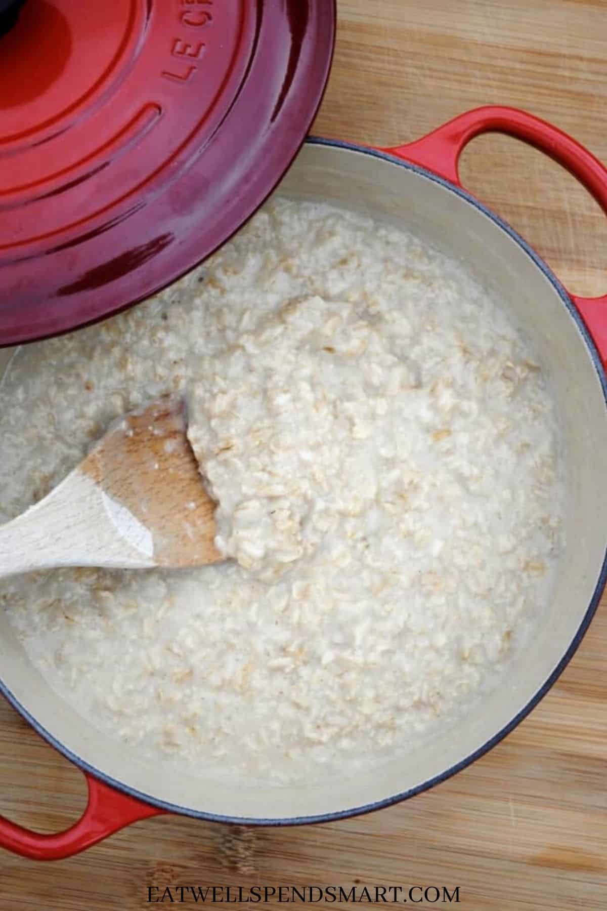 Wooden spoon scooping oatmeal from a red pot.