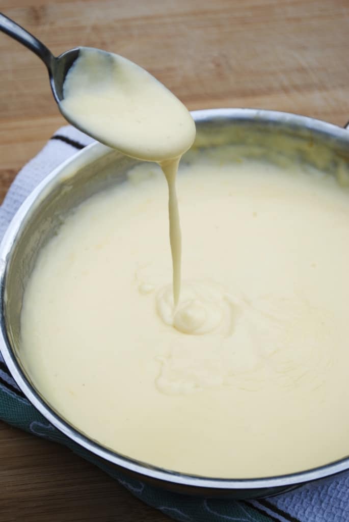 Cheese sauce dripping from a spoon into a skillet