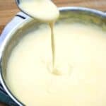 cheese sauce dripping from a spoon into a pan of cheese sauce