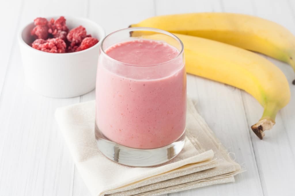 raspberry banana smoothie on a napkin with bananas and raspberries in the background