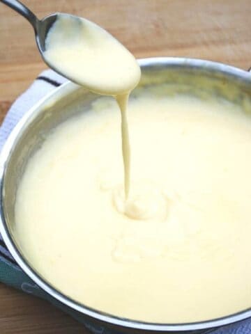 Cheese sauce dripping from a spoon into a skillet of cheese sauce