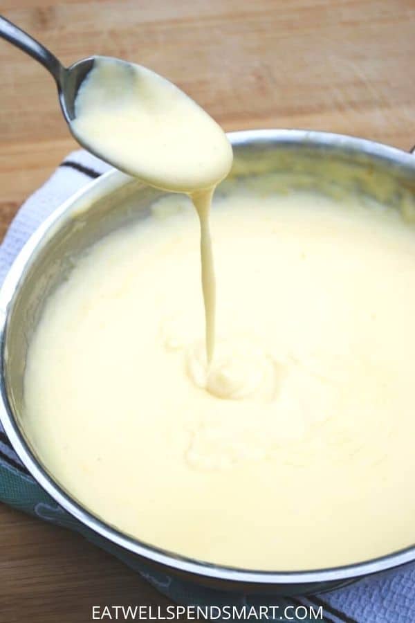 Cheese sauce dripping from a spoon into a skillet of cheese sauce