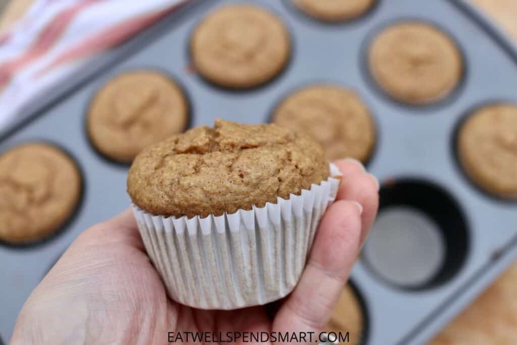 Hand holding an oatmeal muffin with a muffin tin full of muffins in the background