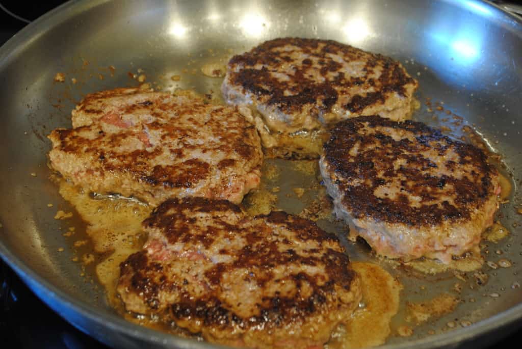 Ground beef patties browning in a skillet.