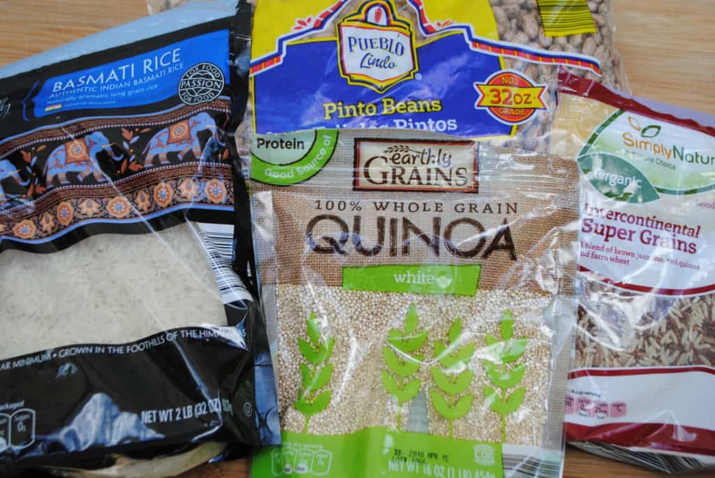 bags of Basmati rice, quinoa, pinto beans, and super grains on a wooden cutting board