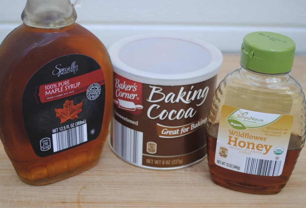 maple syrup, baking cocoa, and honey on a wooden cutting board