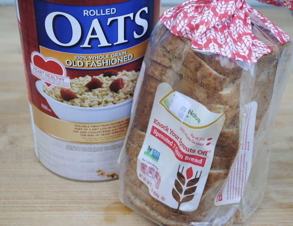 container of old fashioned oats and a loaf of sprouted bread on a wooden cutting board