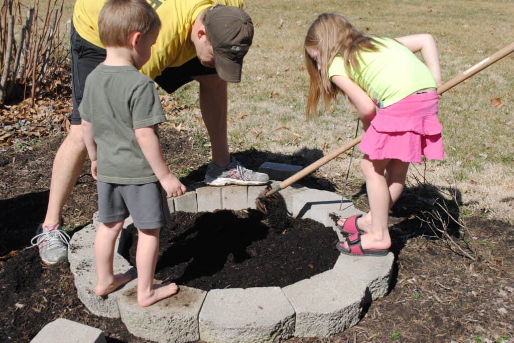 Girl spreading garden soil while man and boy watch