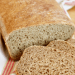 A loaf of homemade bread with two cut bread slices on board