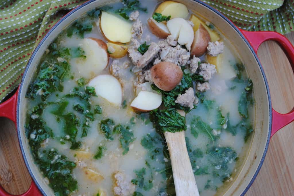 wooden spoon scooping out sausage, kale, and potato soup from a pot