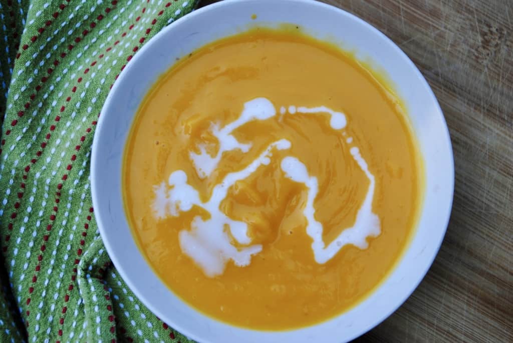 a bowl of butternut squash soup drizzled with coconut milk sitting o a wooden board