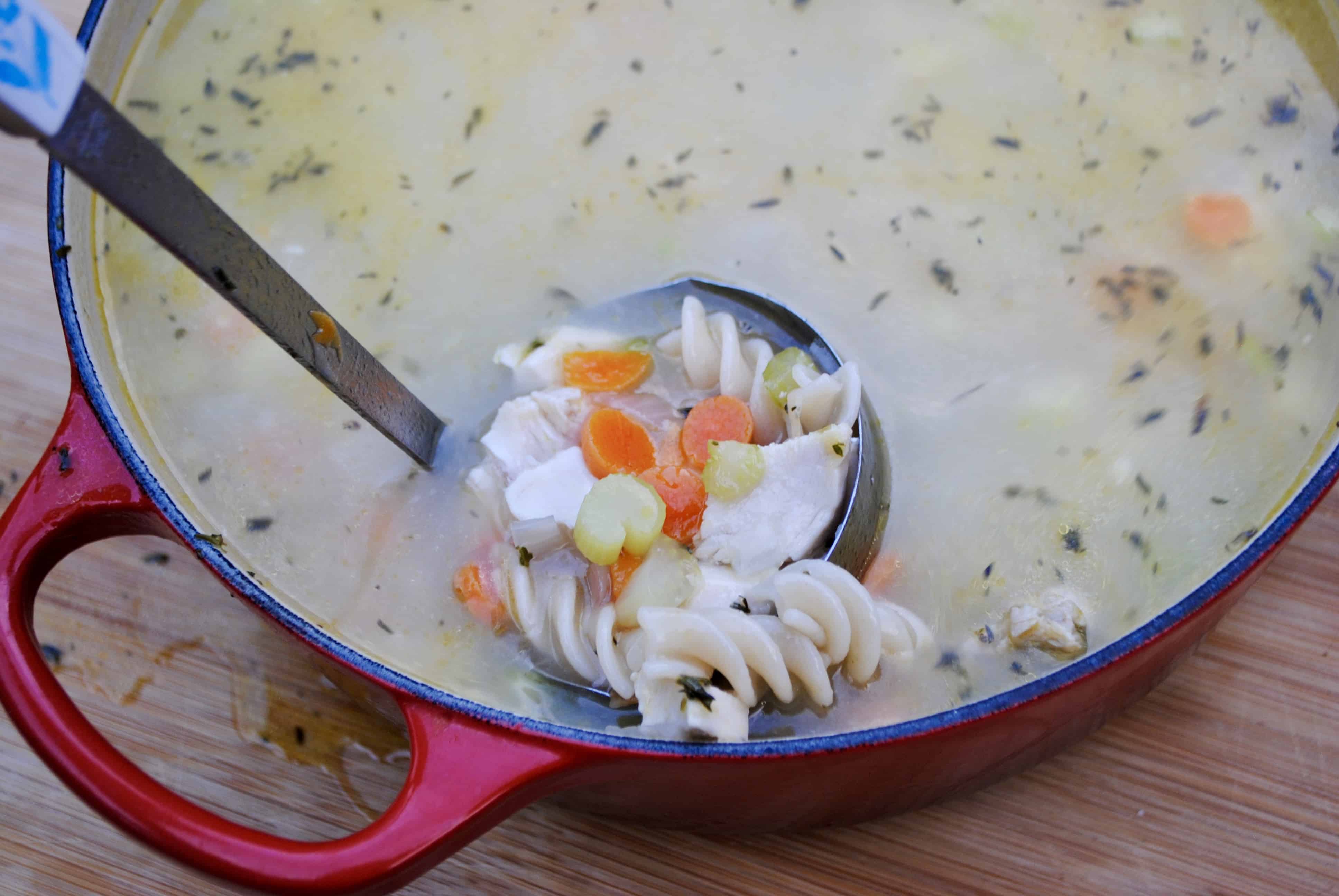 Ladle scooping chicken noodle soup out of a red pot