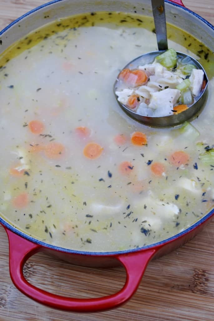 Ladle taking chicken noodle soup out of a red pot