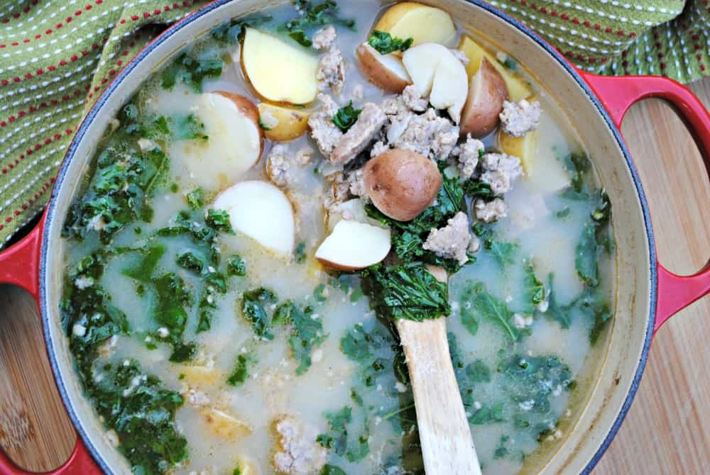 A red stock pot full of Zuppa Toscana: a creamy sausage, kale, and potato soup