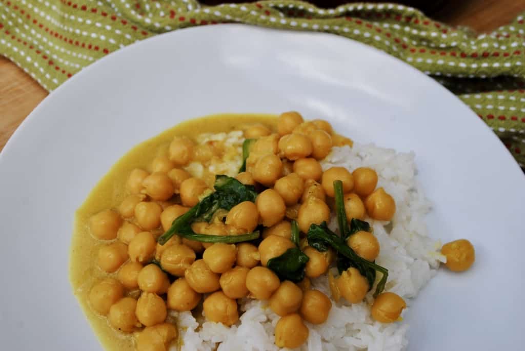 chickpea and spinach curry on a white plate beside a green towel