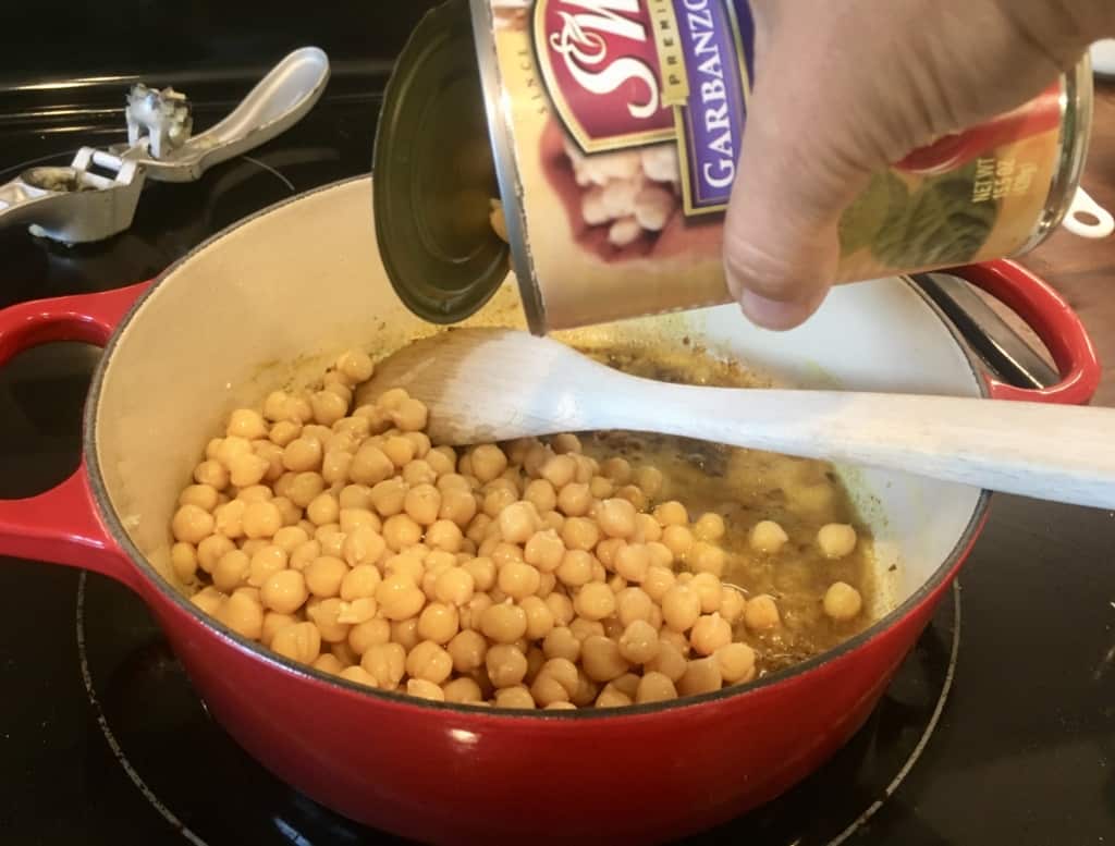 A can of chickpeas being poured into dutch oven.