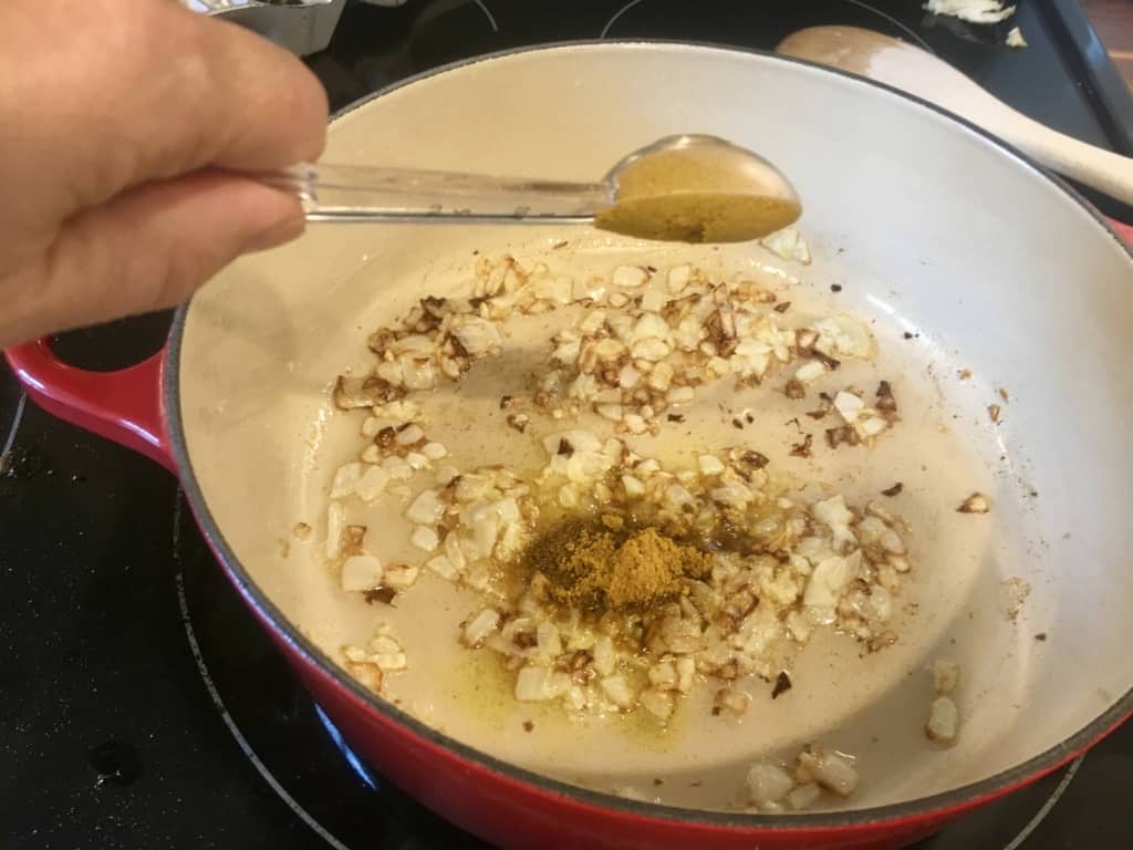 Curry powder being dumped into dutch oven with sautéd onions.