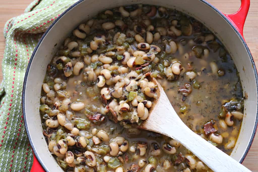 Wooden spoon scooping black eyed peas out of a red stock pot.