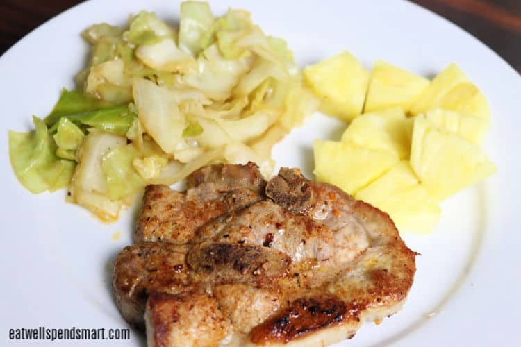 Pork chop, cooked cabbage, and chopped pineapple on a white plate