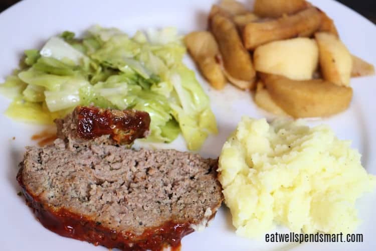 slice of meatloaf, mashed potatoes, cabbage, and baked apples on a white plate