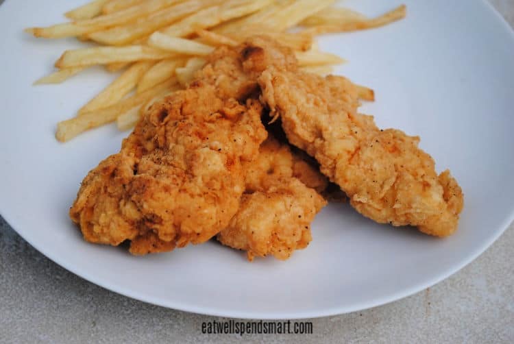 crispy chicken tenders with fries in the background on a white plate