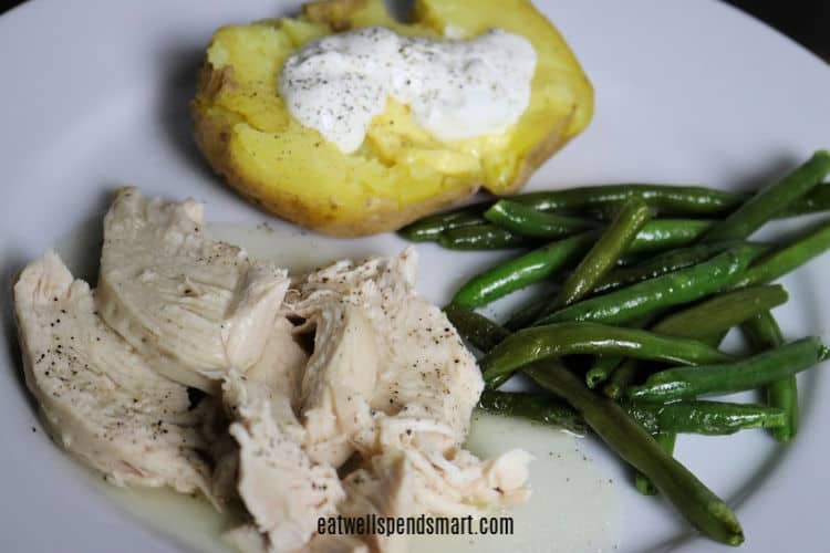 sliced chicken breast with gravy, green beans, and baked potato with butter and sour cream on a white plate