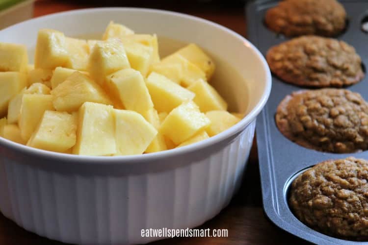 cubed pineapple in a white bowl beside pumpkin oat muffins in a muffin tin