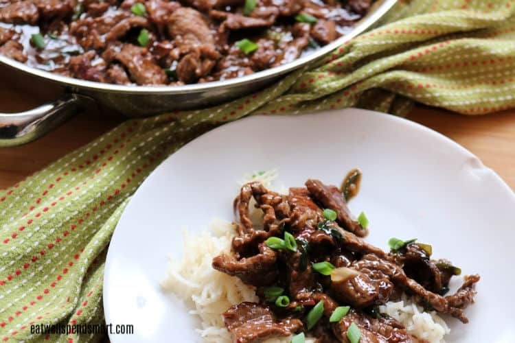 Mongolian beef on rice on a white plate with green towel beside it.