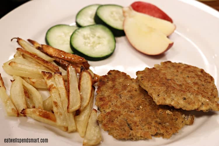 salmon patties, oven fries, apple slices, and cucumber slices on a white plate