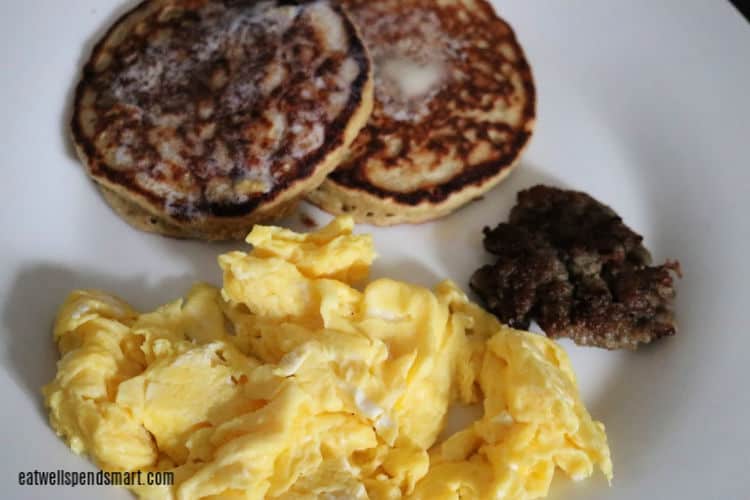 scrambled eggs, sausage, and oat pancakes on a white plate