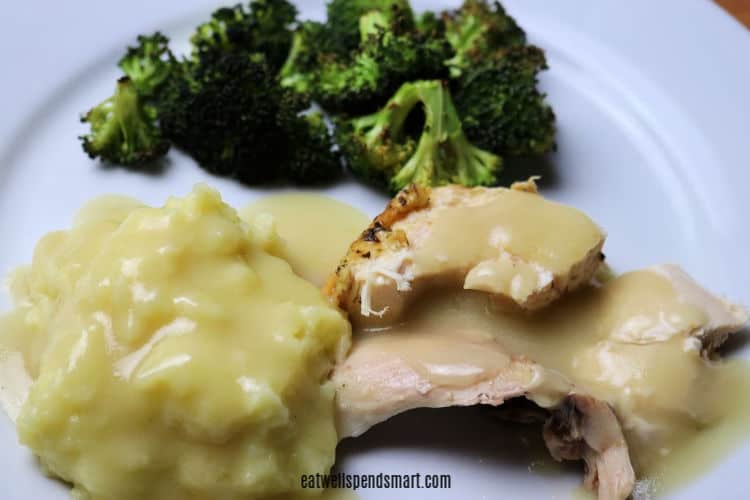 sliced roasted chicken and mashed potatoes covered in gravy with roasted broccoli in the background 