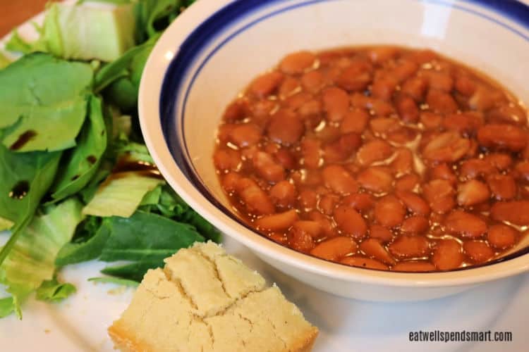 bowl of pinto beans on a white plate with a side salad and cornbread