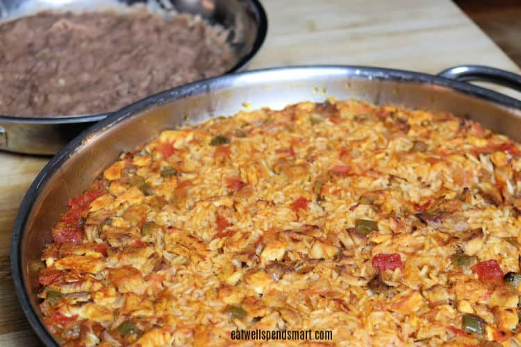 large skillet with Spanish rice and chicken with refried beans in the background