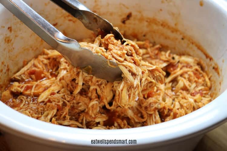 tongs grabbing slow cooker salsa chicken from a white slow cooker