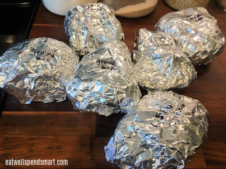 ground beef and chicken breasts wrapped in foil on a wooden countertop