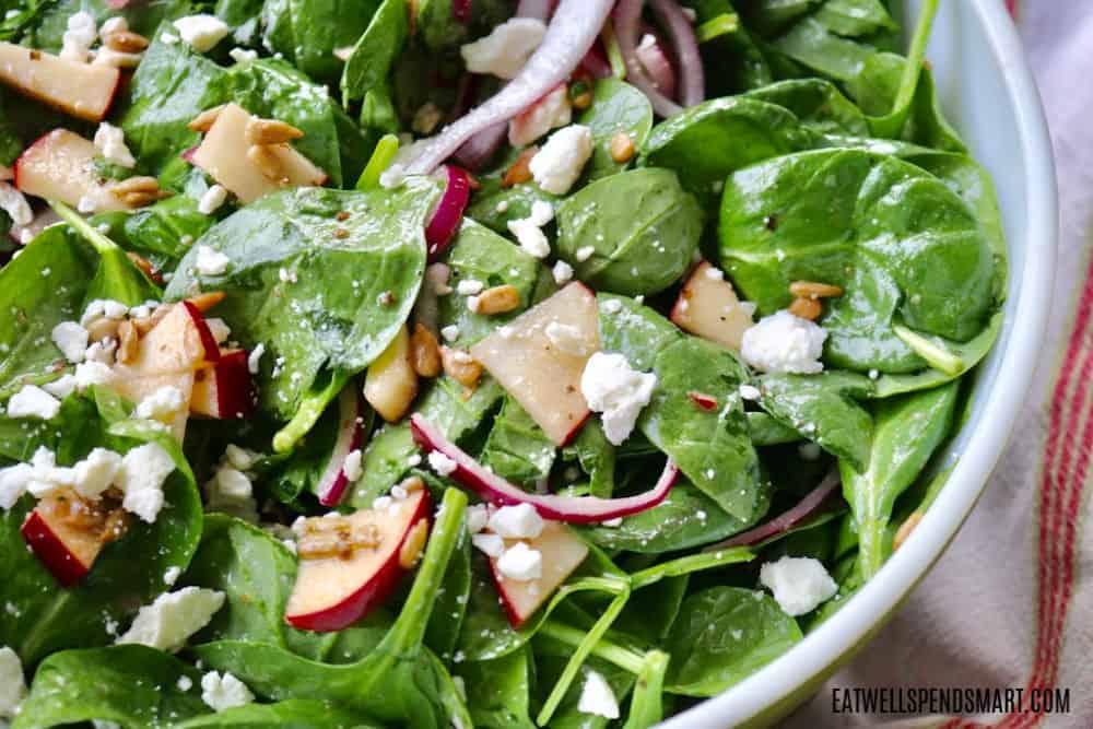 Spinach and apple salad with red onion, feta cheese, and sunflower seeds.