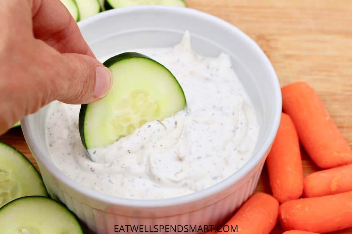 hand dipping a cucumber slice into a white bowl of sour cream dip