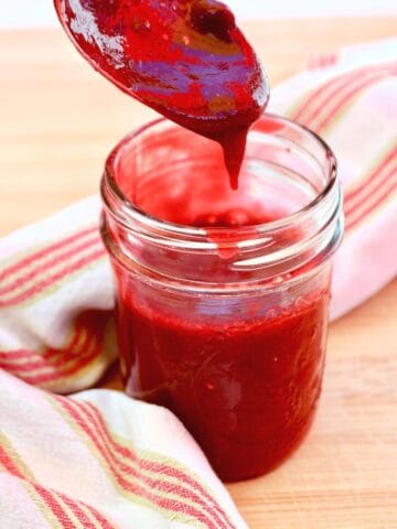 Spoon dripping raspberry sauce into a small jar
