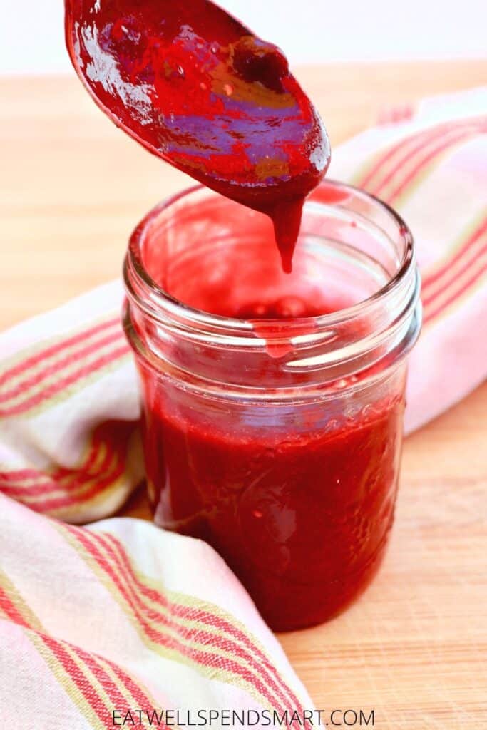 Spoon dripping raspberry sauce into a small jar