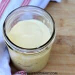 mango banana smoothie in a jar on a wooden board with a white and red striped towel