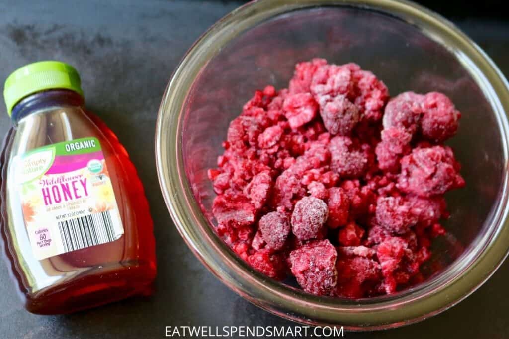 honey and a bowl of frozen raspberries on a dark board
