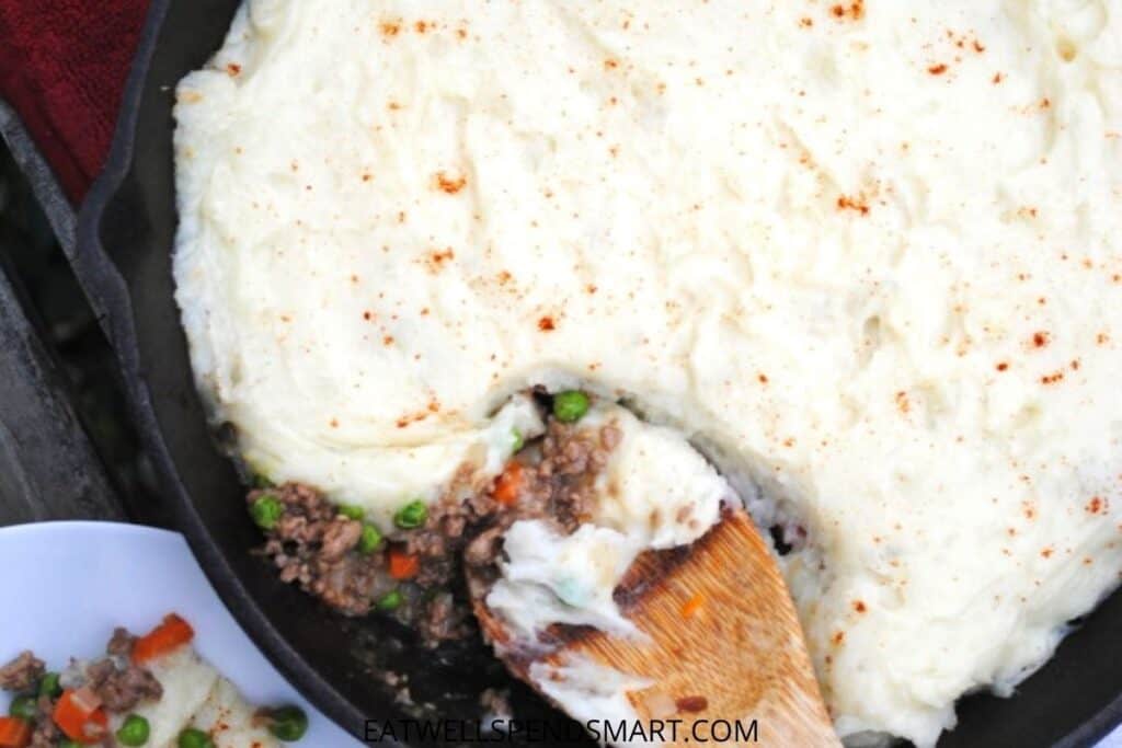 wooden spoon scooping shepherd's pie out of a cast iron skillet
