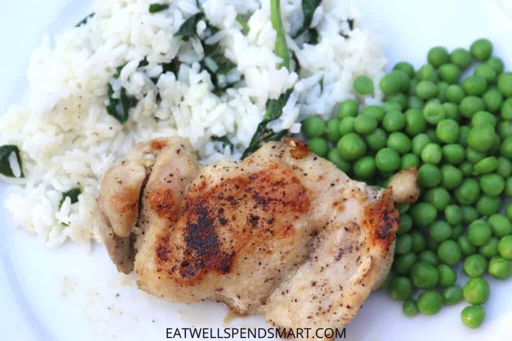 stove top chicken thigh, rice with spinach, and peas on a white plate