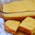 Two slices of homemade cornbread in front of a pan of cornbread